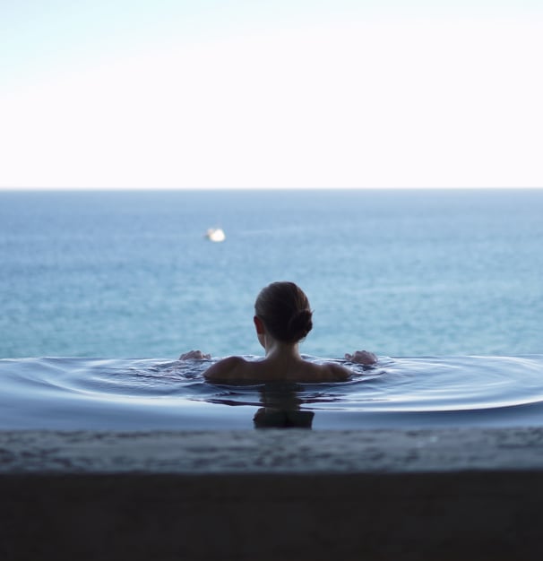 A woman swimming in an infinity pool looking at the sea